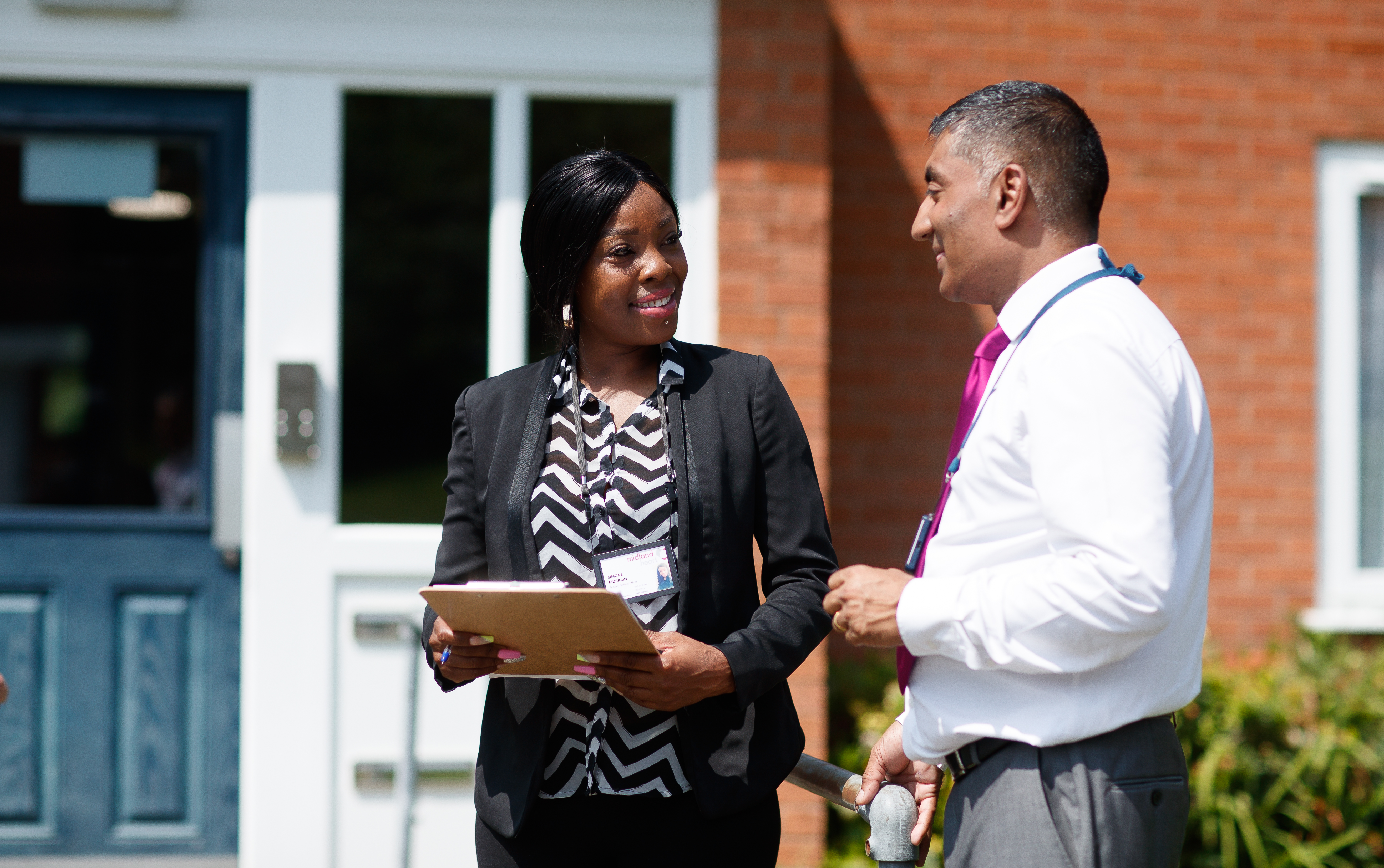 2 Midland Heart employees standing outside homes with a clipboard