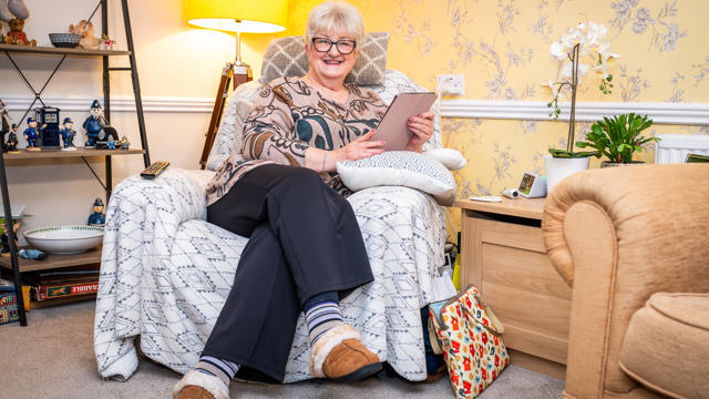 A Tenant Sat In An Armchair Smiling With Her Tablet